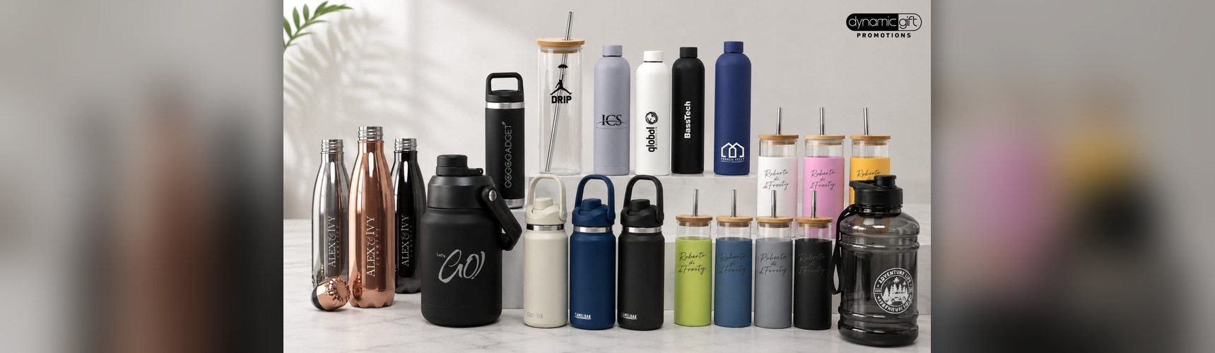 Branded drink bottles, tumblers and glass cups with bamboo lids lined up on a white marble bench